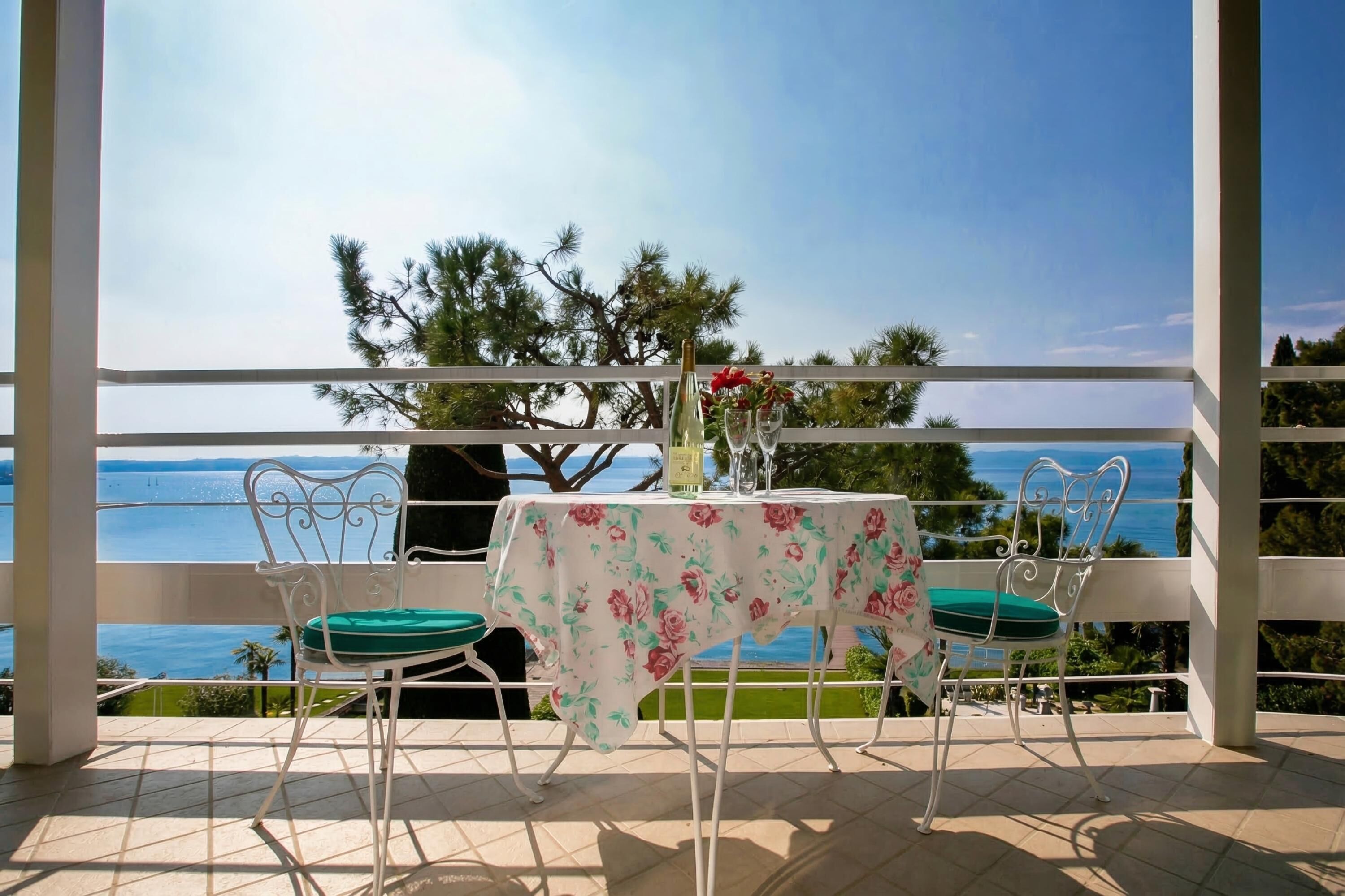 A balcony with a table and chairs, overlooking a body of water and greenery.