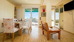 Uma sala de jantar com uma mesa, cadeiras, um relógio vermelho e uma televisão na parede.