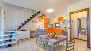 A modern kitchen with orange cabinets, a dining area with a table and chairs, and a staircase with white railings. - Residenza Verde (Desenzano del Garda)
