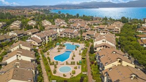 An aerial view of a residential area with multiple apartment buildings, a central swimming pool, and a lake in the background. - Residenza Verde (Desenzano del Garda)