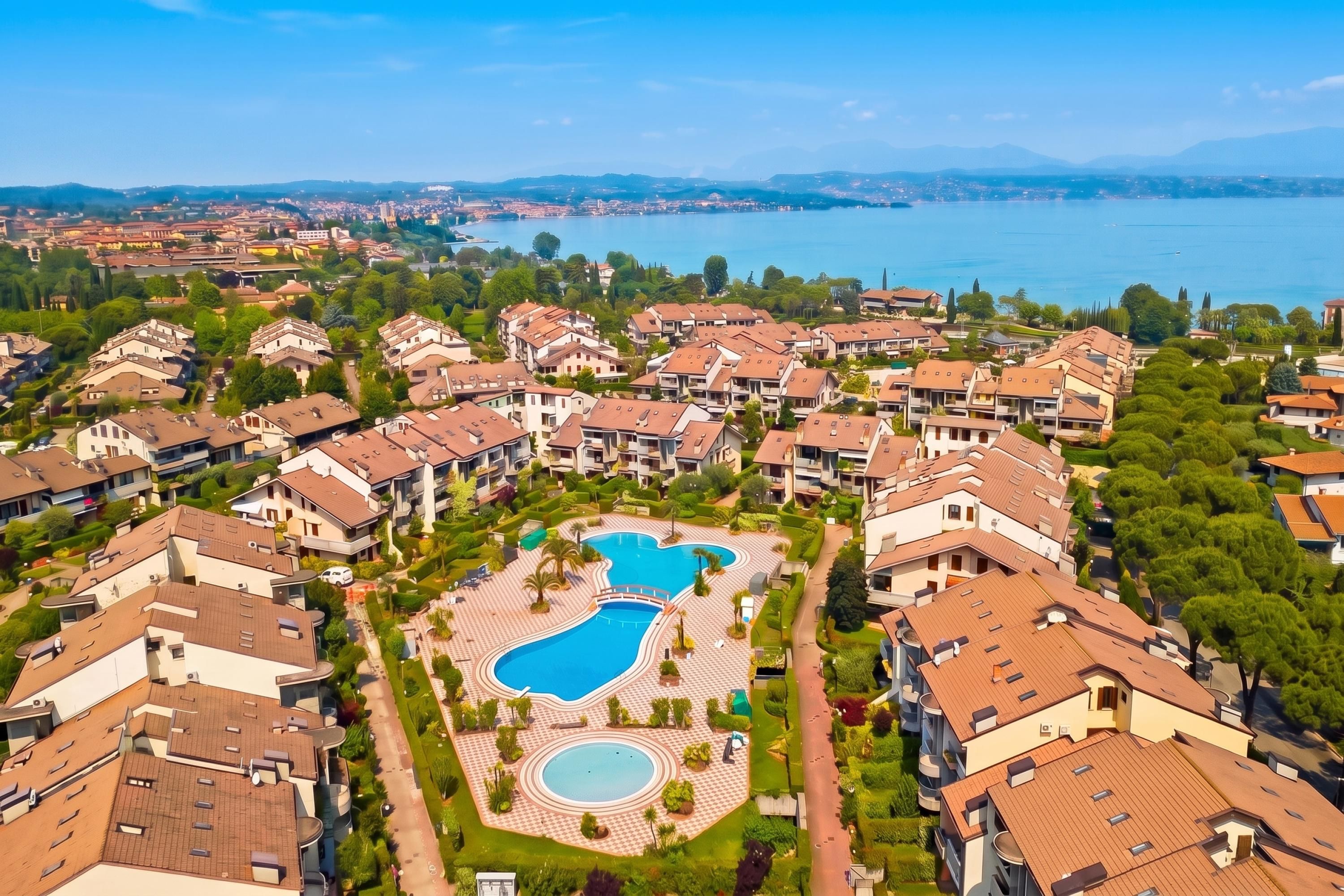 Un quartier résidentiel comprenant plusieurs immeubles d’appartements, une piscine centrale et une vue sur un lac.