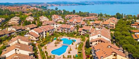 A residential area with multiple apartment buildings, a central swimming pool, and a view of a lake.