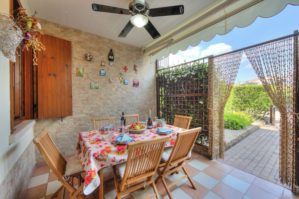 A dining area with a table set for four, surrounded by wooden chairs, a ceiling fan, and a stone wall with various decorations.