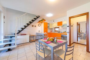 A modern kitchen with orange cabinets, a dining area with a table set for two, and a staircase with a white railing. - Residenza Verde (Desenzano del Garda)