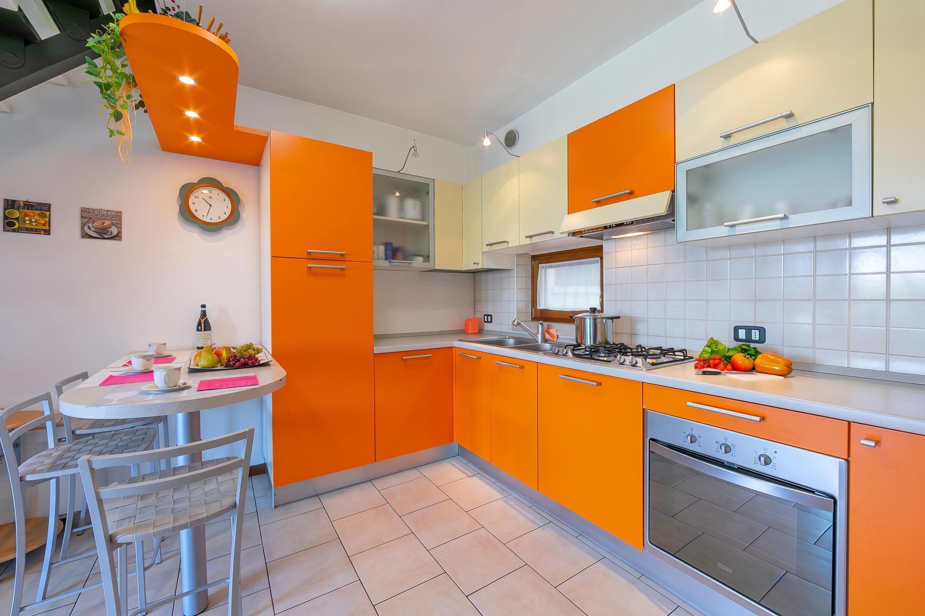 A modern kitchen with orange cabinetry, a stainless steel stove, and a dining area with a table and chairs.