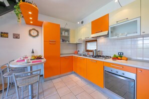 A modern kitchen with orange cabinetry, a stainless steel stove, and a dining area with a table and chairs. - Residenza Verde (Desenzano del Garda)