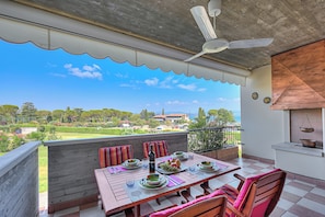 An outdoor dining area with a view of a garden and buildings, a ceiling fan, and a table set with plates and glasses. - Residenza Verde (Desenzano del Garda)