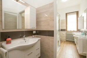 A bathroom with a large mirror, a sink, a toilet, and a shower area. - Villa Alberti Appartamento Emma (Salò)