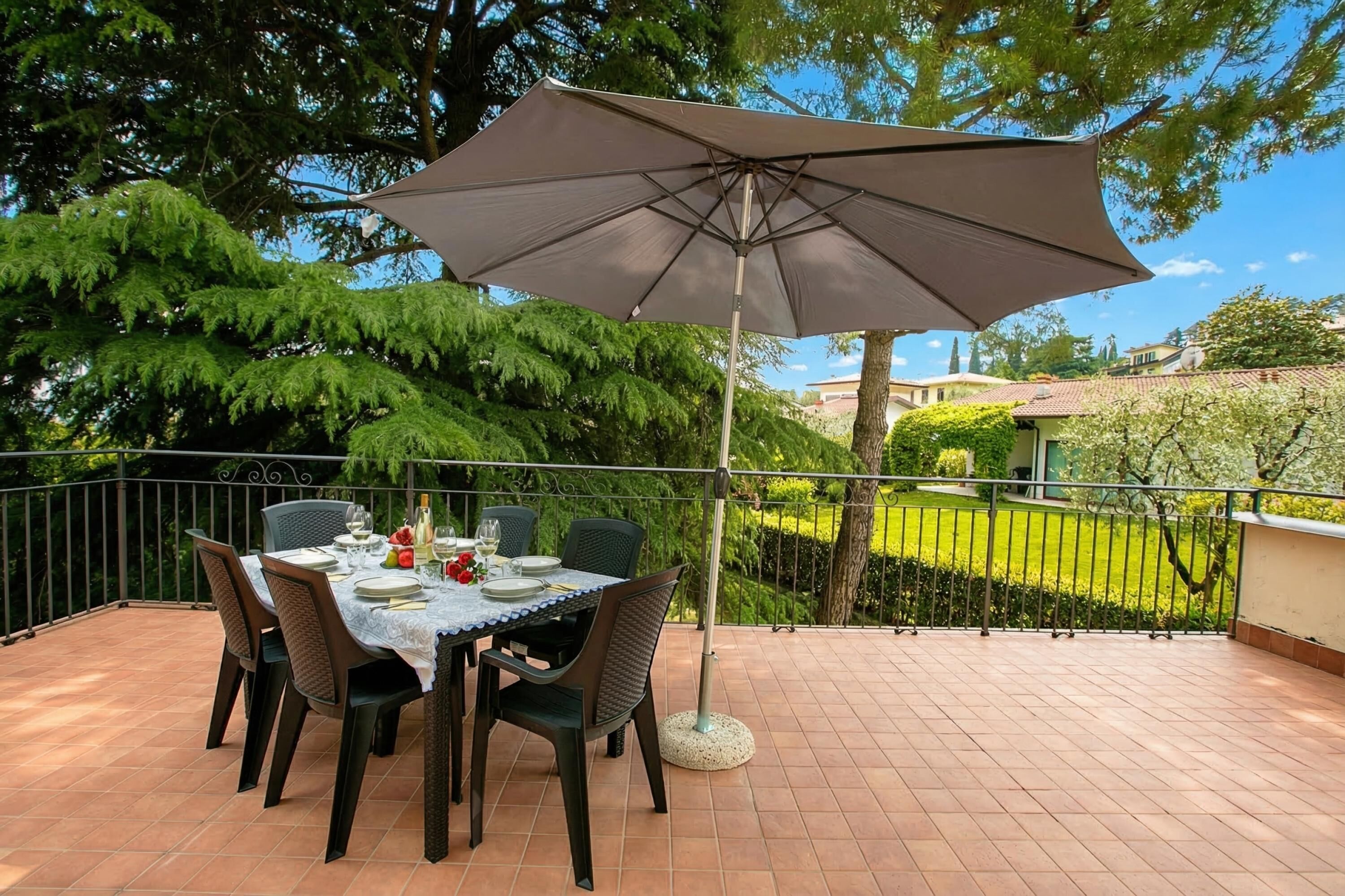 Eine Terrasse im Freien mit einem Essplatz, umgeben von Stühlen und einem Sonnenschirm.