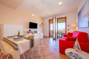A modern living room with a red sofa, a dining area with a table set for four, and a balcony with a view. - Appartamento Vista Lago (Desenzano del Garda)