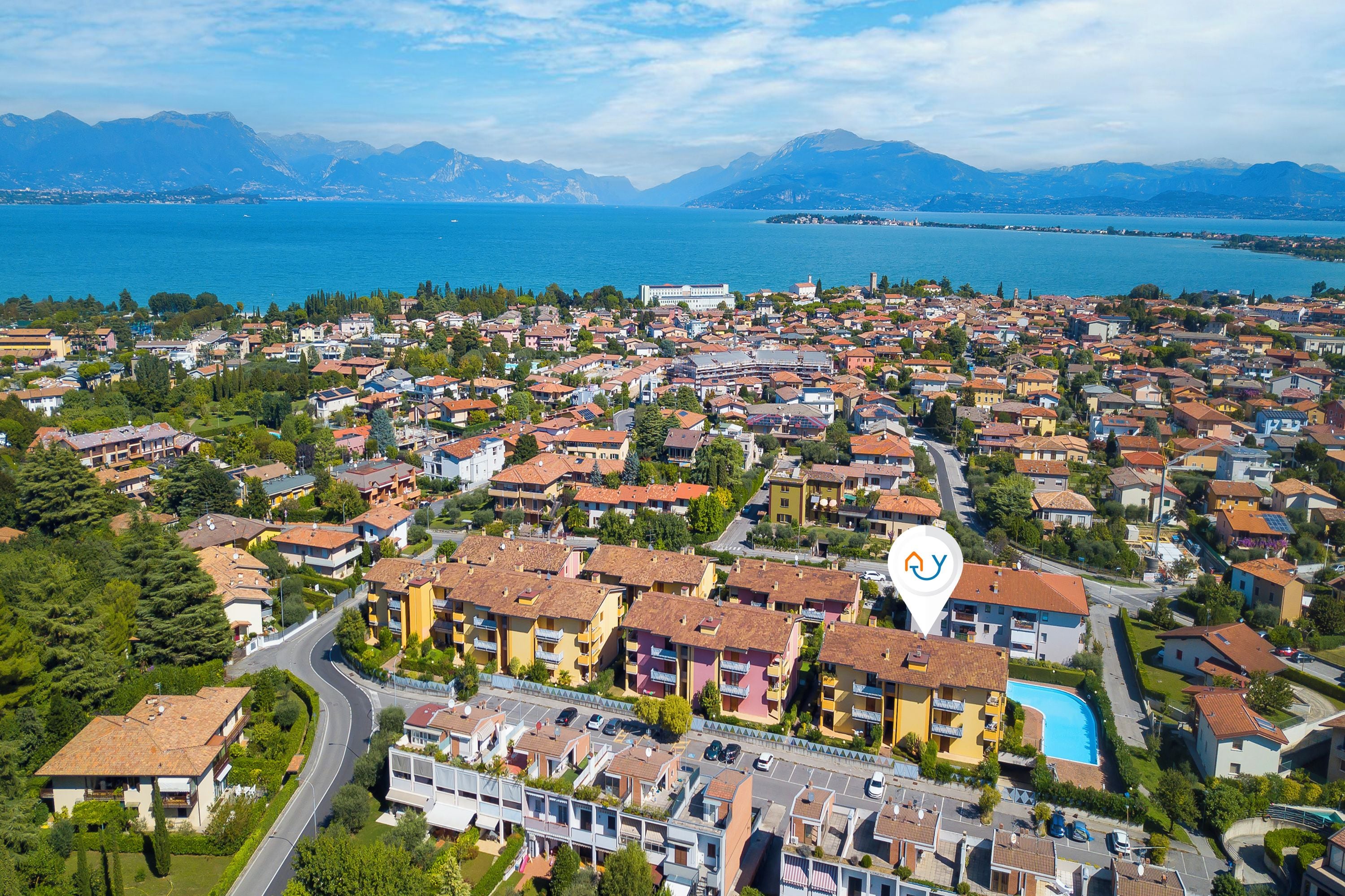 A residential area with a mix of single and multi-story buildings, a swimming pool, and a view of a lake and mountains in the background.