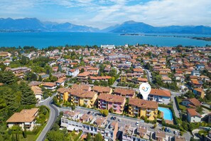 A residential area with a mix of single and multi-story buildings, a swimming pool, and a view of a lake and mountains in the background.