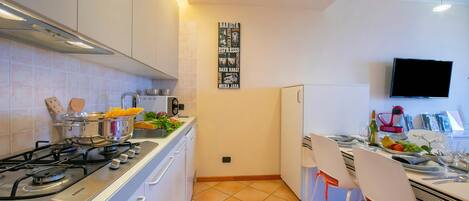 A modern kitchen with a gas stove, white cabinets, a tiled backsplash, a wall-mounted TV, and a dining area with white chairs and a table set for two.