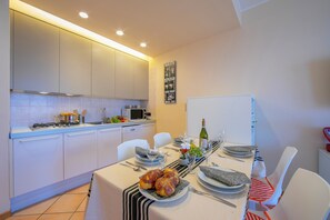 A modern kitchen with white cabinets, a dining table set with plates, glasses, and a bottle of wine. - Appartamento Vista Lago (Desenzano del Garda)