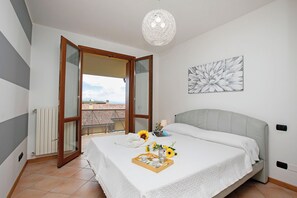 A bedroom with a bed, a bedside table, a nightstand, a window, and a view of the outside.