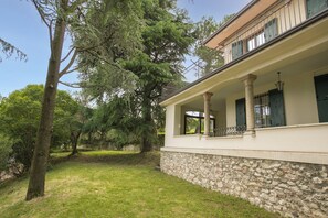 A building with a stone foundation, a balcony with metal railings, and a large tree in the foreground. - Villa Alberti Appartamento Bruna (Salò)
