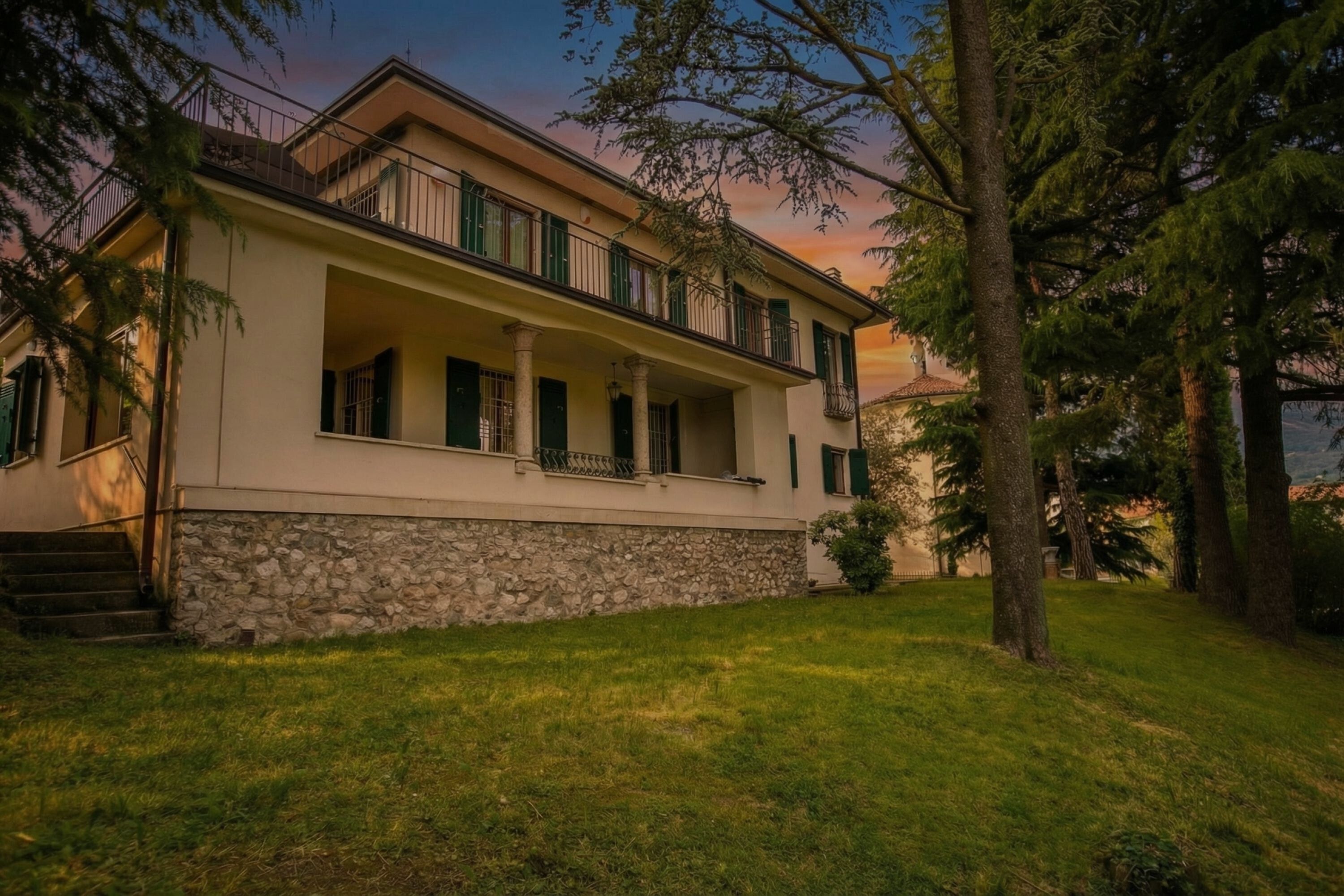 A two-story building with a stone foundation, green shutters, and a balcony.