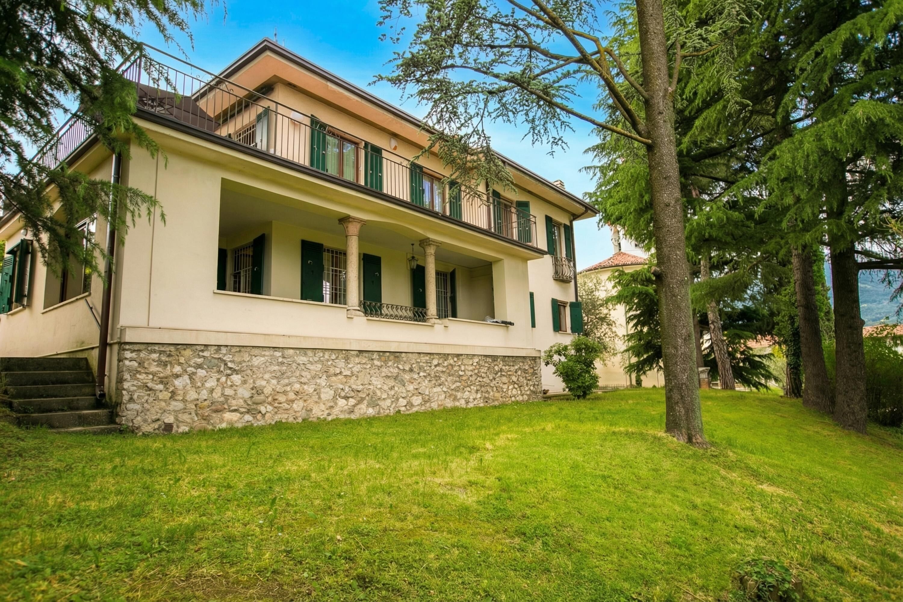 A two-story building with a stone base, a balcony, and a grassy yard.