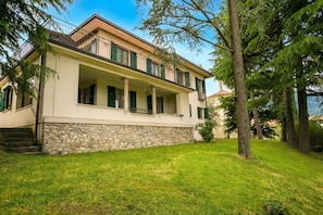 A two-story building with a stone base, a balcony, and a grassy yard.