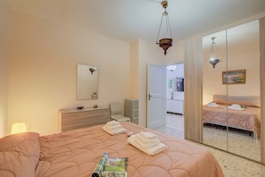 A bedroom with a large bed, a dresser, a mirror, and a door leading to another room.