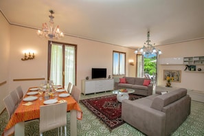 A dining area with a table set for four, a sofa, a TV, and a chandelier.