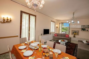 A dining area with a table set for four, a television, a sofa, and a window with curtains.