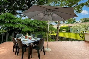 A patio with a table set for dining, surrounded by chairs, and an umbrella providing shade.