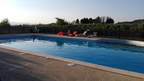 A swimming pool with a tiled edge, surrounded by a fence, and equipped with lounge chairs. - Mas Boheme (Espeluche)