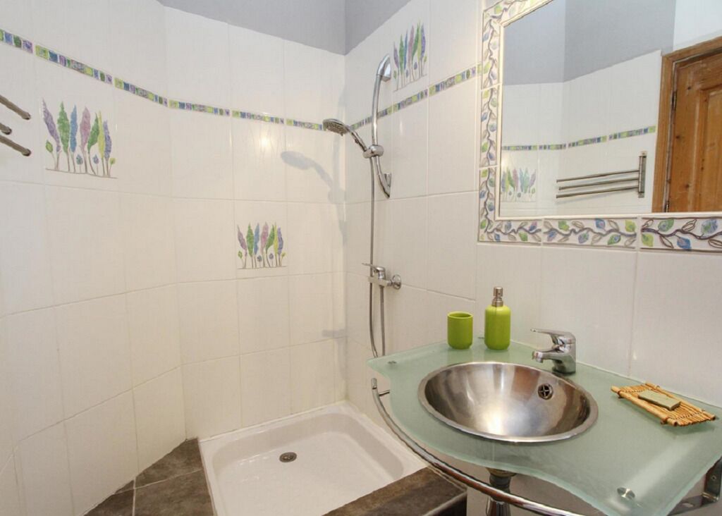 A bathroom with a glass sink, a shower, and decorative tiles.