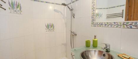 A bathroom with a glass sink, a shower, and decorative tiles.