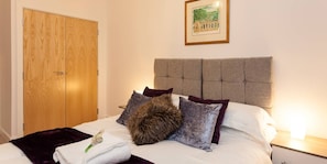 Un dormitorio con un armario de madera, una cama con cabecera gris y un cuadro en la pared.