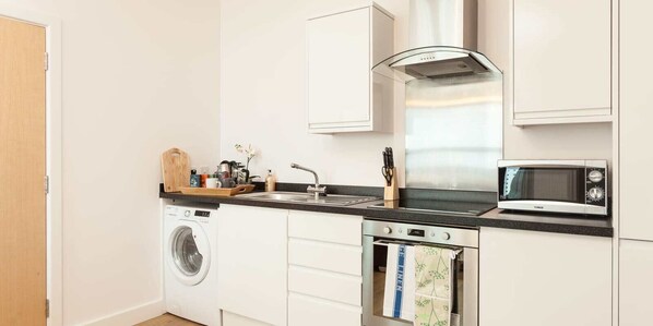 A compact kitchen with a washing machine, oven, microwave, and a sink with a faucet.