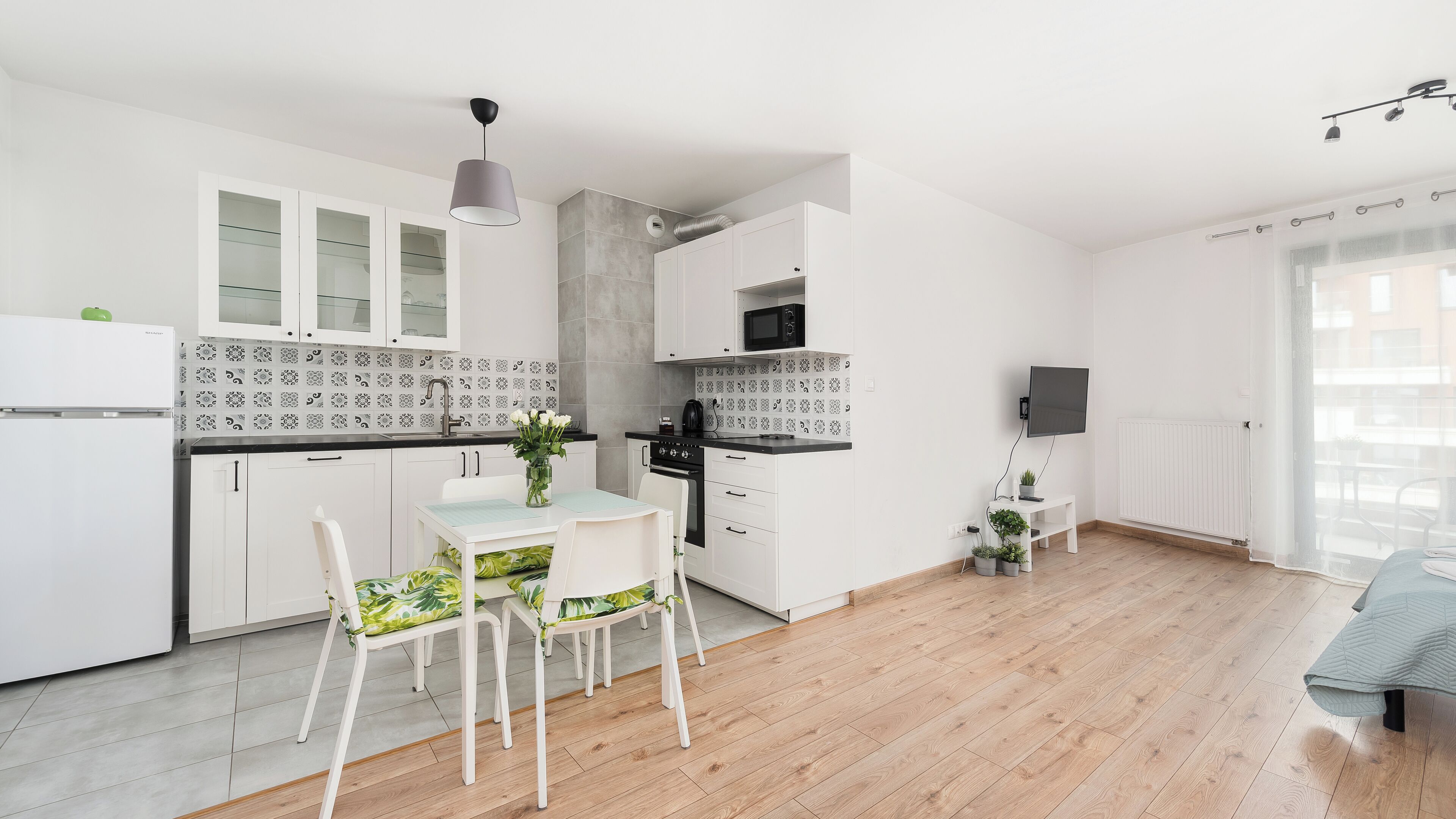A modern kitchen with white cabinets, a black countertop, and a dining area with a table and chairs.