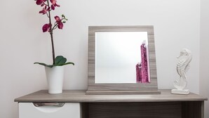 Un espejo en marco sobre un aparador de madera, con una orquídea en maceta y una escultura blanca.