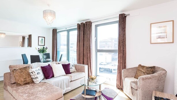 Una sala de estar moderna con un conjunto de sofá, una mesa de centro de vidrio y vistas de la ciudad a través de amplias ventanas.