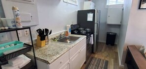 A compact kitchen with a sink, stove, and refrigerator. There is a trash bin and a small table with a chair. - Cozy Tiny Home Near Downtown Lenoir City (Lenoir City)