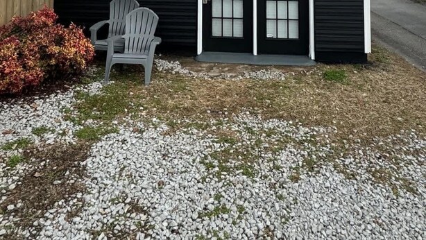 A small, single-story building with a black and white exterior, a garage door, and a small porch area with a chair.
