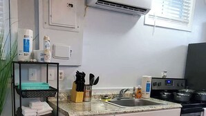 A compact kitchen with white cabinets, a stainless steel stove, and a built-in oven. There is a black shelf with folded towels and a potted plant.