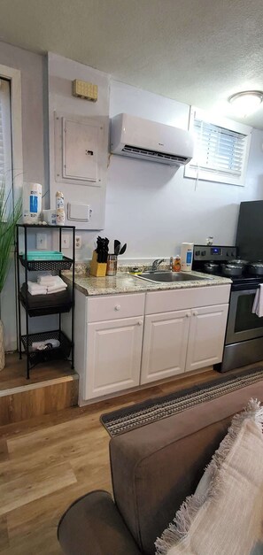 A compact kitchen with white cabinets, a stainless steel stove, and a built-in oven. There is a black shelf with folded towels and a potted plant. - Cozy Tiny Home Near Downtown Lenoir City (Lenoir City)