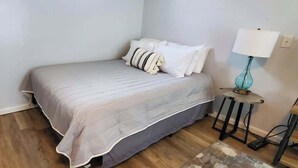 A bedroom with a bed, pillows, a lamp, and a small table.