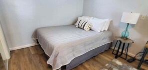 Un dormitorio con cama, almohadas, una lámpara y una mesita.
