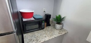 Una cocina con microondas, un tazón rojo, un recipiente azul, una cafetera y una planta en maceta.