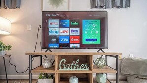 Un televisor sobre un soporte de madera con la palabra “Gather” que muestra diferentes servicios de streaming.