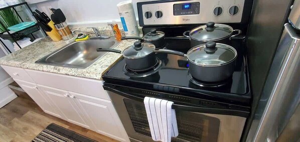 Una cocina con estufa de acero inoxidable, dos ollas, un fregadero y una encimera con diversos utensilios de cocina.