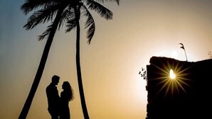 La silhouette d’un couple se découpant sur un coucher de soleil, avec un palmier et un bâtiment illuminé.