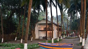 A small house with a balcony, surrounded by palm trees and a colorful boat in the foreground. - 107 - Sand - La Mer Beach House (Revdanda)