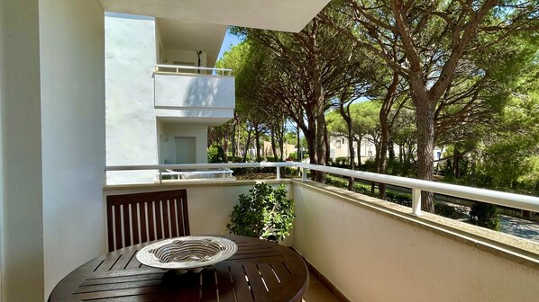 A balcony with a table and chair, a railing, and a view of trees and buildings. - GREEN MAR F 205 (Pals)