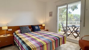 A bedroom with a bed, two bedside tables with lamps, a window with a view of the outdoors, and a sliding glass door leading to an outdoor seating area. - GREEN MAR F 205 (Pals)