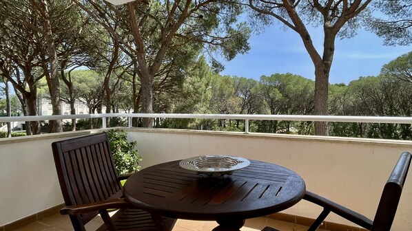 A balcony with a round table and two chairs, overlooking a forested area.