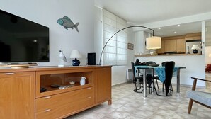 Ein modernes Wohnzimmer mit Fernseher, Holzschrank, Esstisch, Stühlen und einer Küche im Hintergrund.